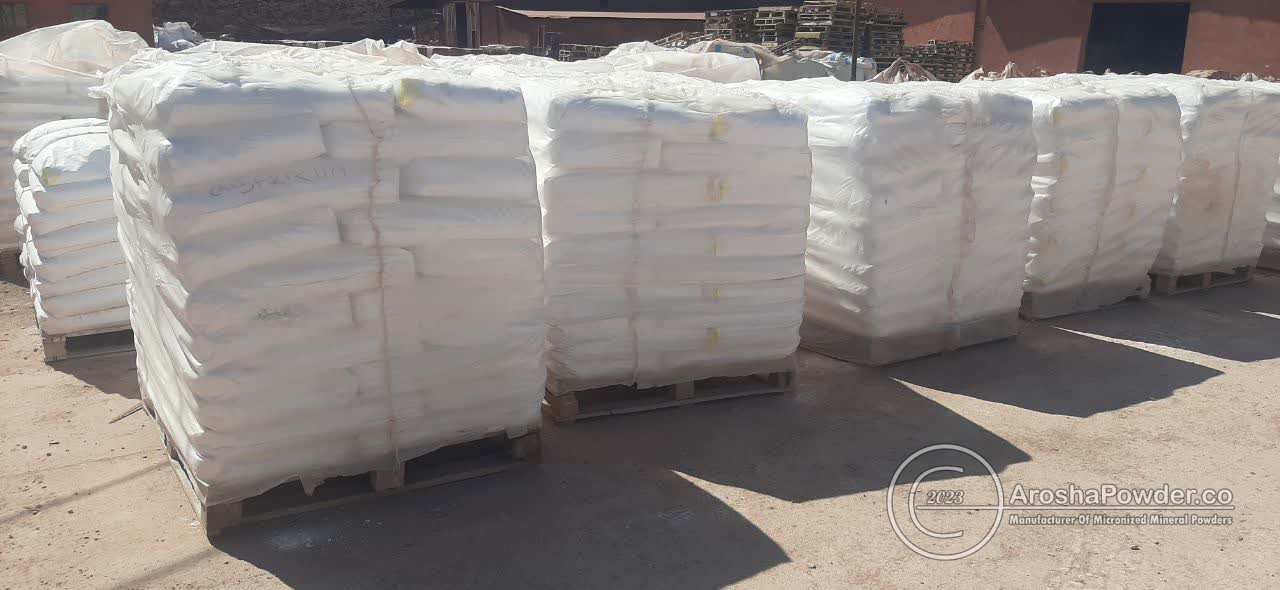 Several tall pallets stacked with white industrial bags stored outdoors in sunlight.